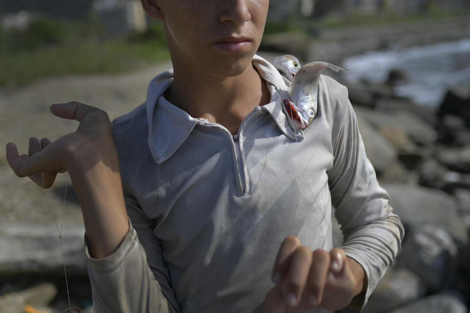 A boy helps Eric Mendez, a 40-year-old bricklayer by trade, with fish Mendez caught in the open sea on his inner tube armed with a hook and line, at Playa Escondida in La Guaira, Venezuela, Friday, Aug. 14, 2020, amid the new coronavirus pandemic. Fishermen like Mendez face strong currents, sharks and the fear a fishhook could puncture their inner tube far from shore. But a day’s catch could feed their families for a week. (AP Photo/Matias Delacroix)