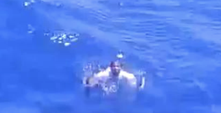 In a grainy snapshot from a video, a fisherman in the water is seen raising his hands up.
