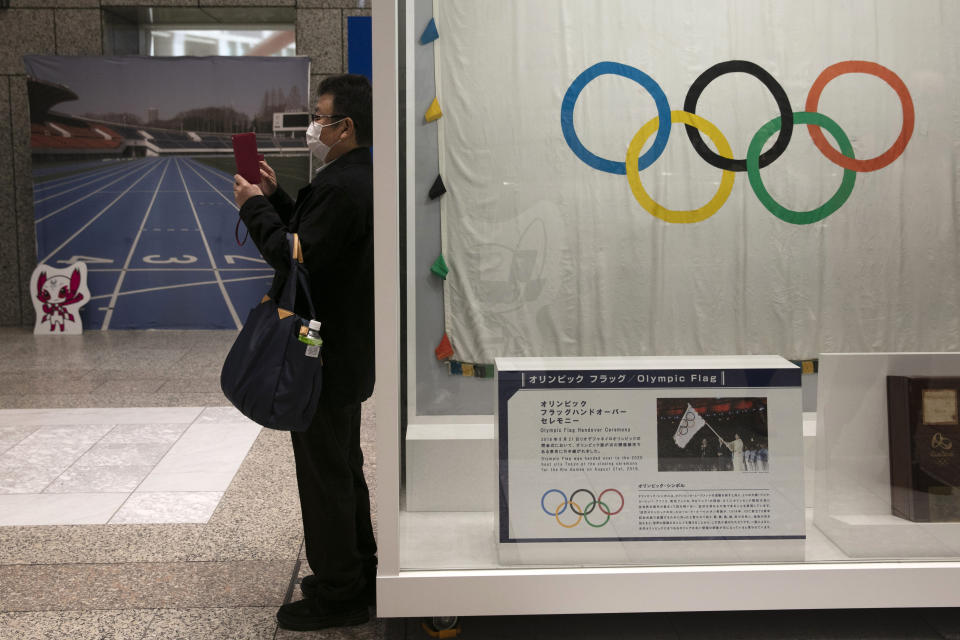 FILE - In this Feb. 18, 2020, file photo, a man wearing a mask takes pictures of the mascots for the Tokyo 2020 Olympics and Paralympics in Tokyo. The spreading virus from China has put the Tokyo Olympics at risk. The Olympics are to open on July 24 - less than five months away. IOC President Thomas Bach declined to speculate about a postponement, cancellation, or any combination of those possibilities. (AP Photo/Jae C. Hong, File)