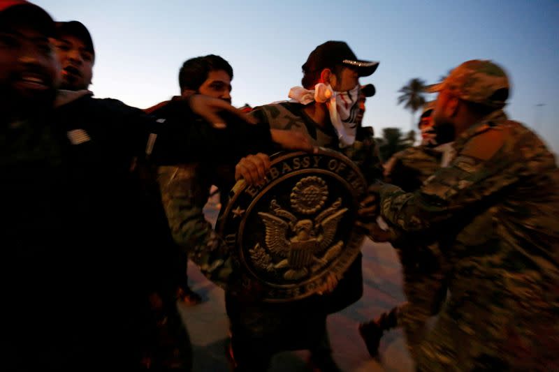 FILE PHOTO: Protesters and militia fighters carry the logo of the U.S. Embassy, during a protest to condemn air strikes on bases belonging to Hashd al-Shaabi (paramilitary forces), in Baghdad