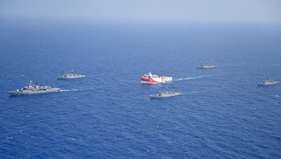 In this photo provided by the Turkish Defense Ministry, Turkey's research vessel, Oruc Reis, in red and white, is surrounded by Turkish navy vessels as it was heading in the west of Antalya on the Mediterranean, Turkey, Monday, Aug 10, 2020. Tension remains high between Greece and Turkey, whose warships are in the eastern Mediterranean where Turkey has sent a research vessel to carry out seismic research for energy resources in an area Greece says is on its continental shelf.(Turkish Defense Ministry via AP, Pool)