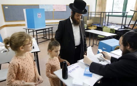 Children accompany an ultra-Orthodox Jewish man to a voting station in the city of Bnei Brak during the Israeli parliamentary election - Credit: &nbsp;MENAHEM KAHANA/&nbsp;AFP