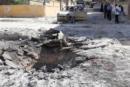 A crater is pictured as people inspect a site hit by air strikes in Idlib city, Syria July 20, 2016. REUTERS/Ammar Abdullah