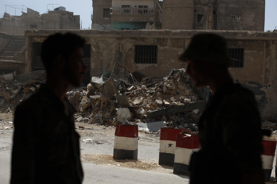 In this July 15, 2018 photo, Syrian soldiers speak as they stand at a checkpoint in the town of Douma, in the eastern Ghouta region, near the Syrian capital Damascus, Syria. The fate of activist Razan Zaitouneh is one of the longest-running mysteries of Syria’s civil war. There’s been no sign of life, no proof of death since gunmen abducted her and three of her colleagues from her offices in the rebel-held town of Douma in 2013. Now Douma is in government hands and clues have emerged that may bring answers. (AP Photo/Hassan Ammar)