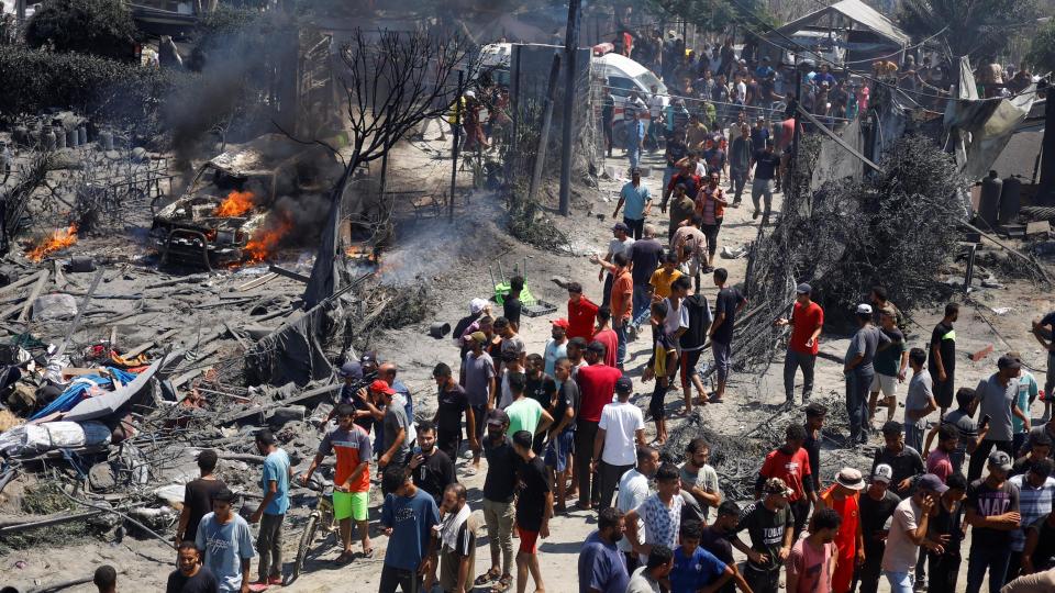 People look at the aftermath of an Israeli air strike in Gaza. A burning car can be seen on the left of the picture.