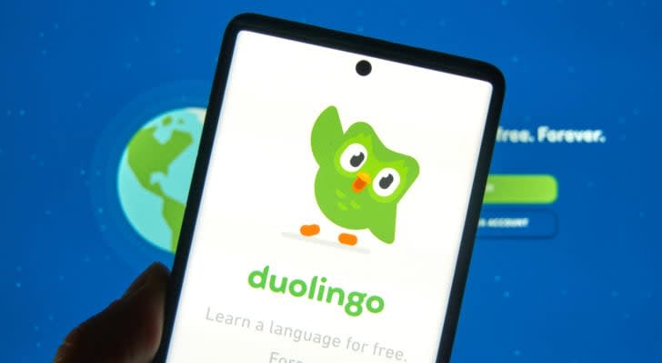 DUOL stock: A phone displaying the duolingo logo in front of a computer screen displaying the duolingo site