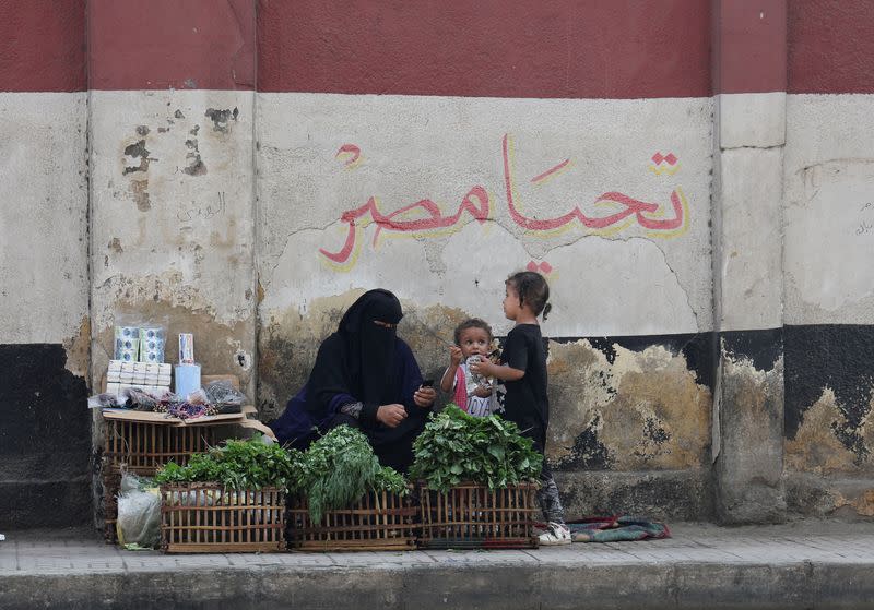 FILE PHOTO: A woman street vendor with her children sits in front of a wall painting featuring the Egyptian national flag and text that reads "Long live Egypt" as she waits for customers in Cairo