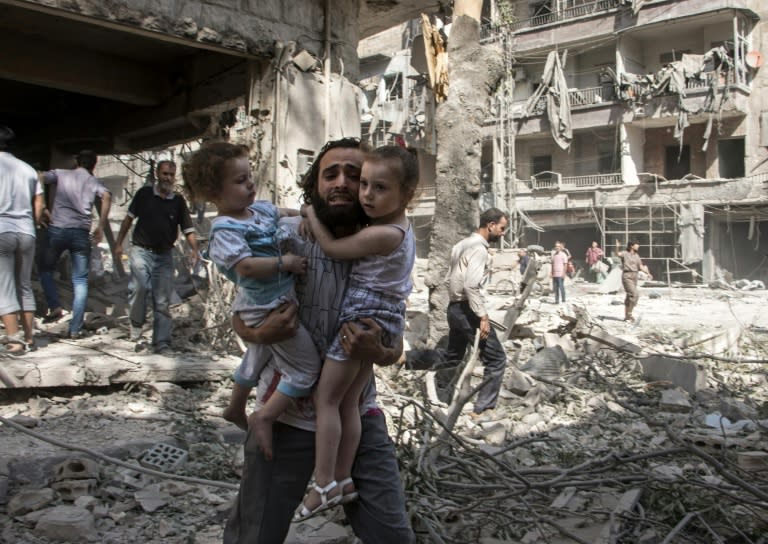 A Syrian man carries two girls as he walks across the rubble following a barrel bomb attack on the rebel-held neighbourhood of al-Kalasa in the northern Syrian city of Aleppo on September 17, 2015