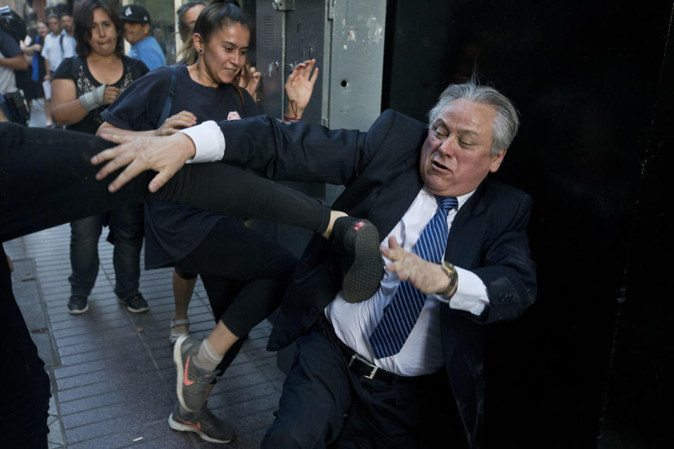 Ivan Arostica, president of Chile's Constitutional Court, ties to avoid a kick by a protester as he leaves the court, which listened to arguments in favor and against conditional freedom for those convicted of human rights crimes, in Santiago, Chile, on Wednesday, Dec. 19, 2018. Protesters fear a ruling in favor could benefit the prisoners of Punta Peuco, a prison for state agents convicted of murder during the 1973-1990 dictatorship of Augustus Pinochet. (AP Photo/Esteban Felix)