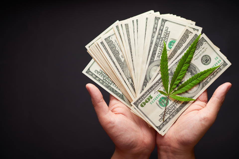 Hands holding $100 bills and a marijuana leaf.