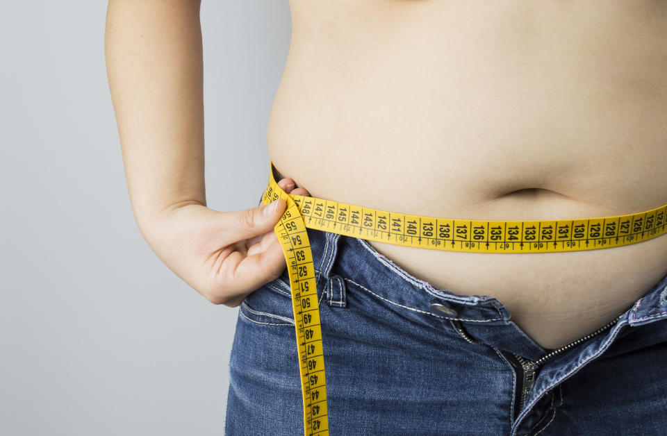 obese woman measuring her waist with a measuring tape against a white background