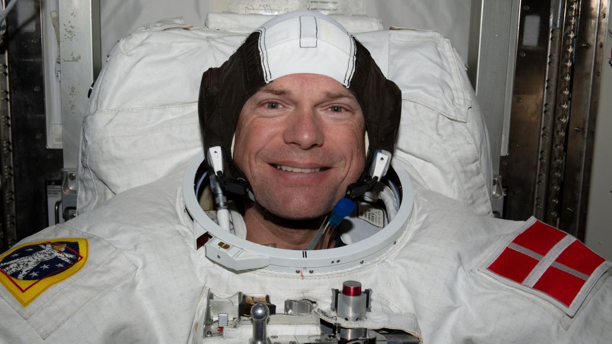  An astronaut smiles in a white spacesuit bearing the red and white flag of Denmark. 