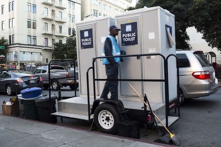 An attendant stands outside two portable toilets in the Tenderloin District in San Francisco, California December 30, 2014. REUTERS/Stephen Lam