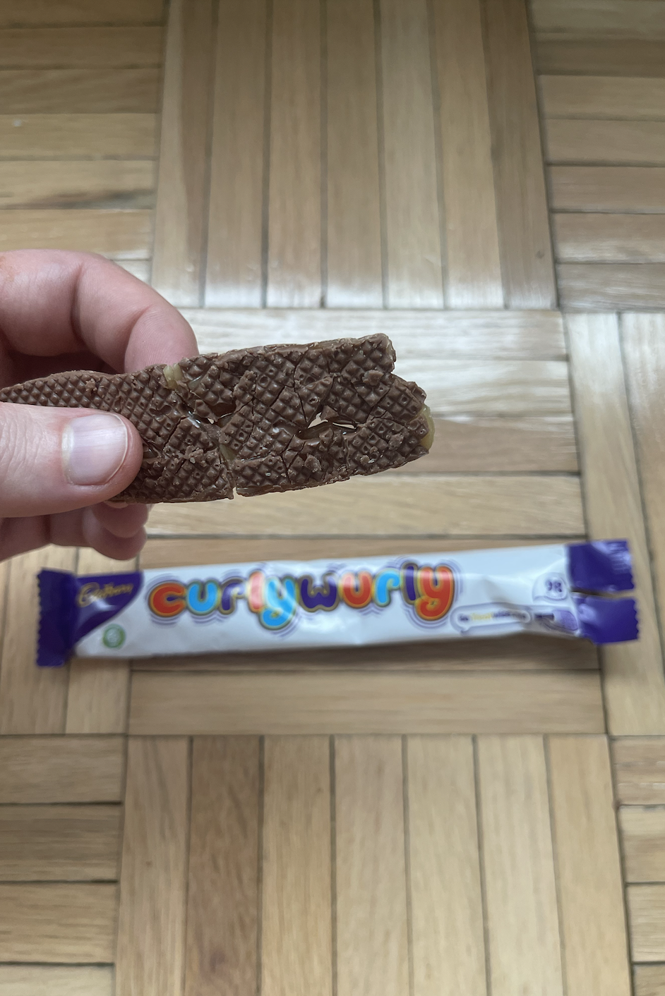 Hand holding a Curly Wurly chocolate bar with a piece broken off, showing the interior, with an unopened bar below