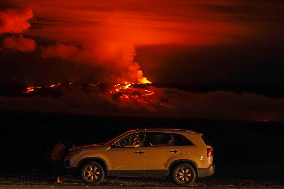 FILE - A man talks on a phone in his car alongside Saddle Road as the Mauna Loa volcano erupts Wednesday, Nov. 30, 2022, near Hilo, Hawaii. Officials monitoring the Mauna Loa eruption on Hawaii's Big island said Wednesday, Dec. 7, the lava flow moving toward state Route 200 has slowed. They said they could not predict when, where or if the lava flow would cross the highway. (AP Photo/Gregory Bull, File)