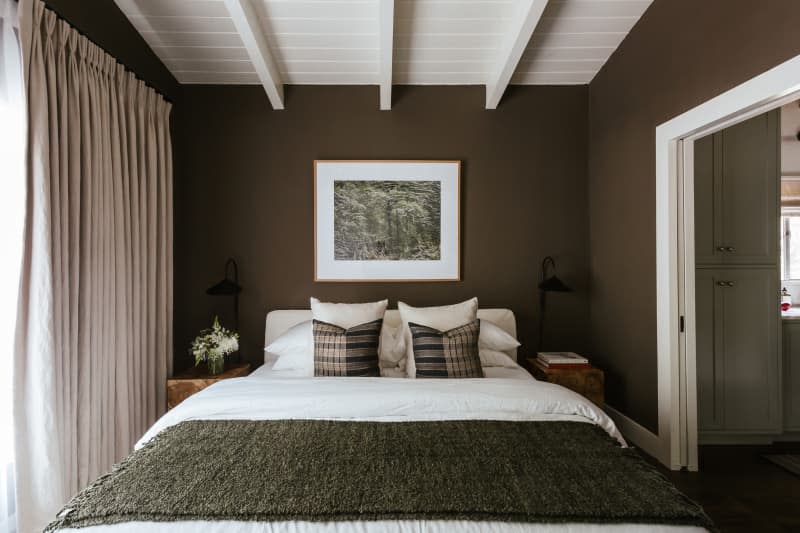 Dark green walls, white tongue and groove with beams, dark green throw blanket, floor to ceiling beige curtains