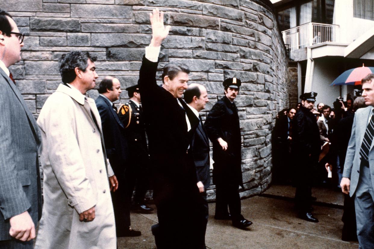 President Ronald Reagan waving to the crowd on March 30, 1981, just before the assassination attempt on him, after a conference outside the Hilton Hotel in Washington, D.C.. Also seriously injured was press secretary James Brady (just behind the car).