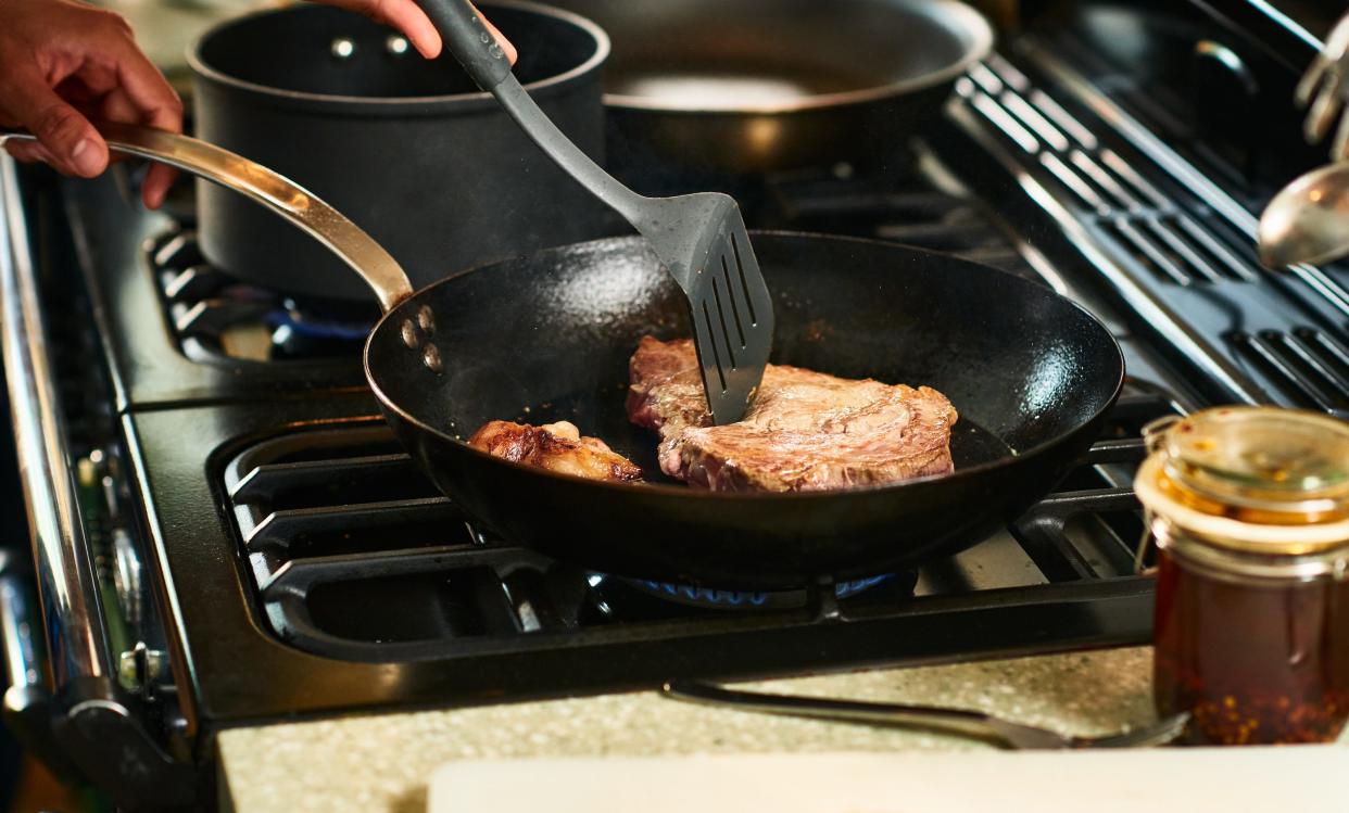 Person using spatula to cook steak in frying pan