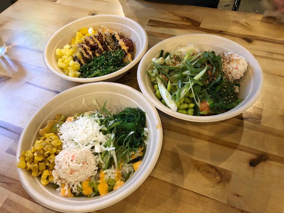 Three poke bowls sit on a wooden table at Poke Papa