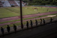 Students do their gymnastics homework on the bleachers of the Pedro Marrero stadium while they watch as a group of teenagers train soccer in Havana, Cuba, Wednesday, Sept. 14, 2022. An initial group of 16 coaches were recently trained by international FIFA officials with the aim to create Cuba's next generation of professional soccer players on an island long known for birthing baseball and boxing superstars. The aim is for Cuba to qualify for the World Cup in the next six to eight years. (AP Photo/Ramon Espinosa)