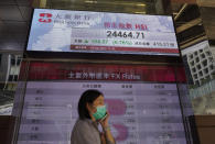 A woman wearing face mask walks past a bank electronic board showing the Hong Kong share index at Hong Kong Stock Exchange Tuesday, April 28, 2020. Asian shares are mixed Tuesday as governments inch toward letting businesses reopen and central banks step in to provide cash to economies. (AP Photo/Vincent Yu)