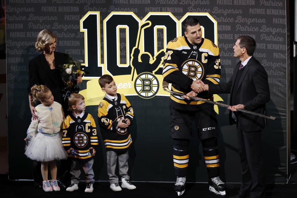 Boston Bruins general manager Don Sweeney, right, presents Patrice Bergeron with a golden hockey stick in celebration of his 1,000 career points as Bergeron's family looks on before an an NHL hockey game against the Columbus Blue Jackets, Saturday, Dec. 17, 2022, in Boston. (AP Photo/Michael Dwyer)