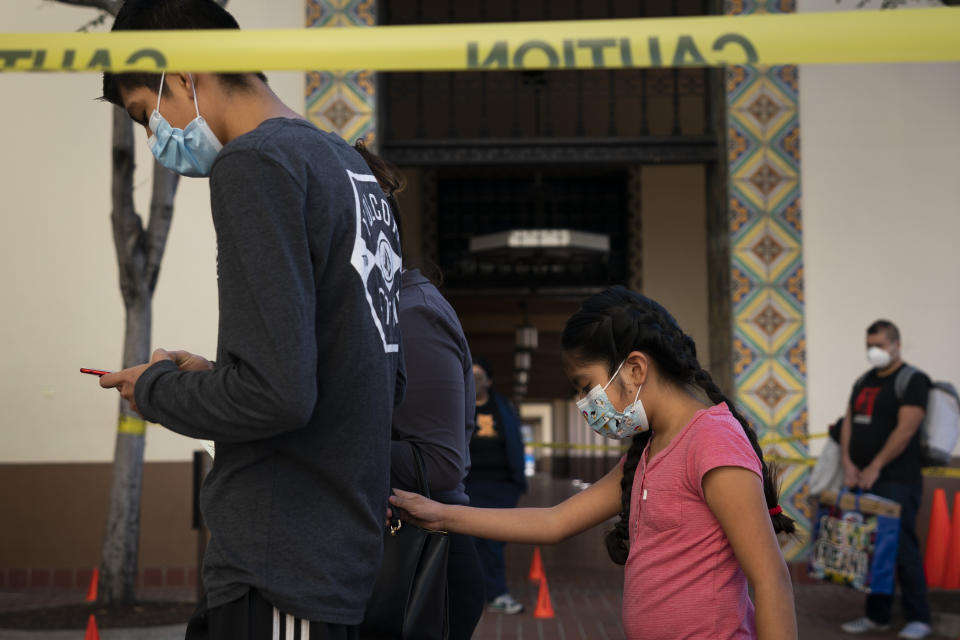 FILE - In this Dec. 9, 2020 file photo Hailey Campos, right, grabs her mother's handbag while waiting in line for a COVID-19 test at a testing site in Los Angeles. California became the first state to record 2 million confirmed coronavirus cases, reaching the milestone on Christmas Eve as close to the entire state was under a strict stay-at-home order and hospitals were flooded with the largest crush of cases since the pandemic began. (AP Photo/Jae C. Hong,File)