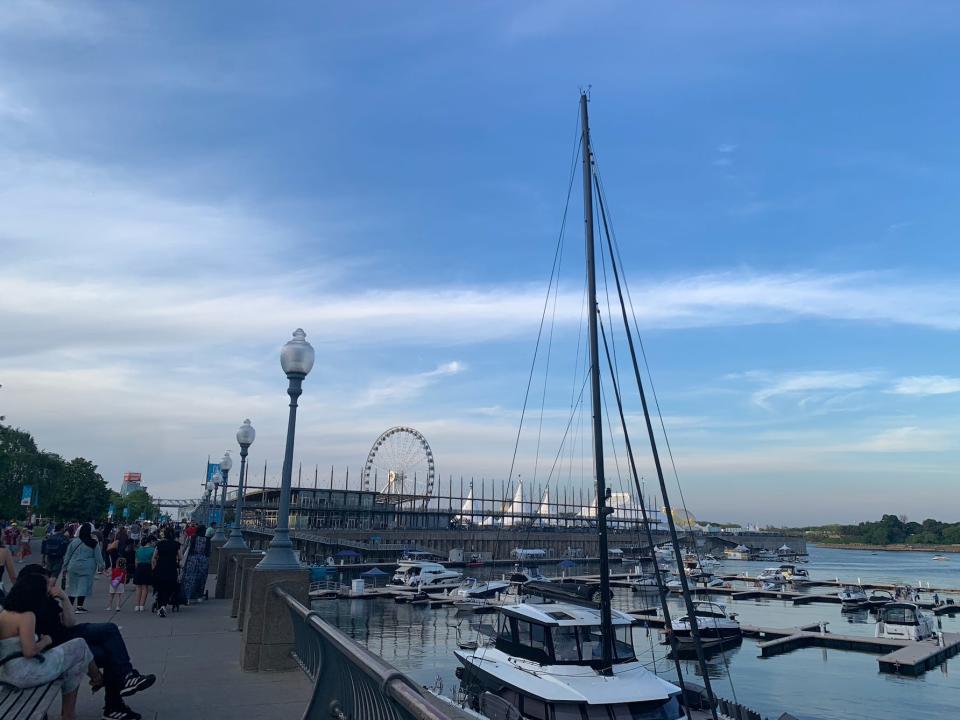 view of the boardwalk in montreal with boats in the water and the ferris wheel in the distance