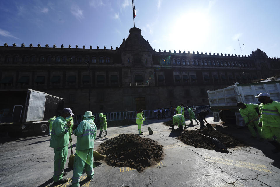 City workers remove piles of dirt symbolizing clandestine graves that were placed by people who have missing family members who demand answers from the government outside the National Palace in Mexico City, Monday, Dec. 13, 2021. (AP Photo/Marco Ugarte)