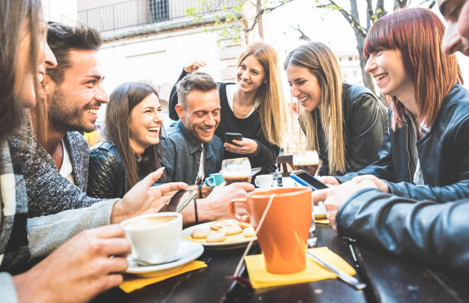 Men and women sharing drinks at a coffee bar while smiling, laughing, and looking at their smartphones