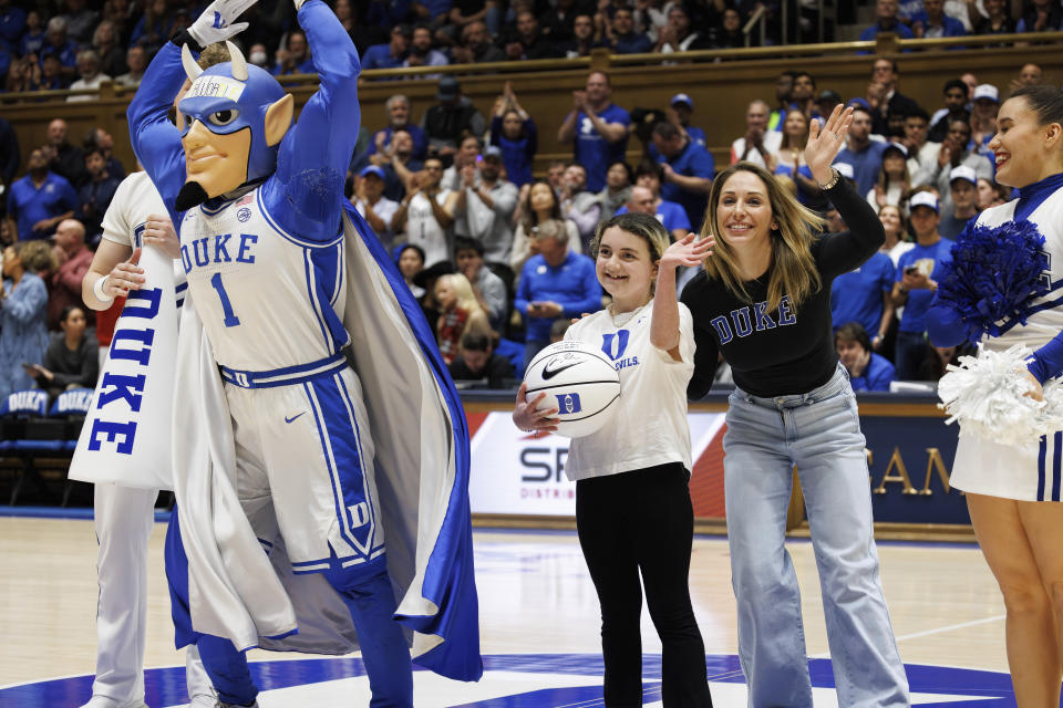 Marcelle Scheyer, center right, wife of Duke coach Jon Scheyer, waves after presenting a basketball signed by coach Scheyer to Samantha DiMartino, center, as an honoree of the Scheyer Family Kid Captain Program, which recognizes patients and families of Duke Children's Hospital, during a timeout in an NCAA college basketball game between Duke and Louisville in Durham, N.C., Wednesday, Feb. 28, 2024. (AP Photo/Ben McKeown)