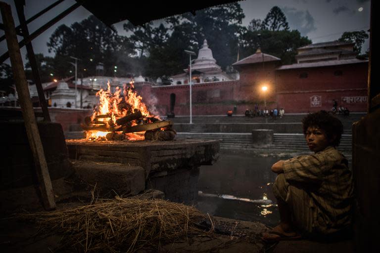A Nepalese Hindu boy sits near a funeral pyre as a body is cremated in Kathmandu on May 2, 2015