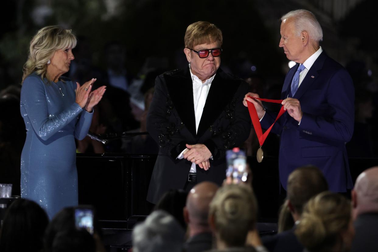 U.S. President Joe Biden (R) presents British singer-songwriter Sir Elton John (2nd L) with the National Humanities Medal as first lady Jill Biden (L) looks on during an event on the South Lawn of the White House on September 23, 2022 in Washington, DC.