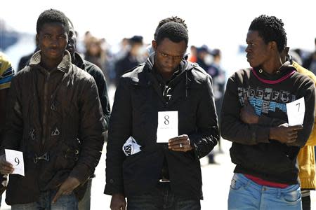 Migrants hold their identification numbers as they arrive at the Sicilian port of Augusta near Siracusa March 21, 2014. REUTERS/Antonio Parrinello