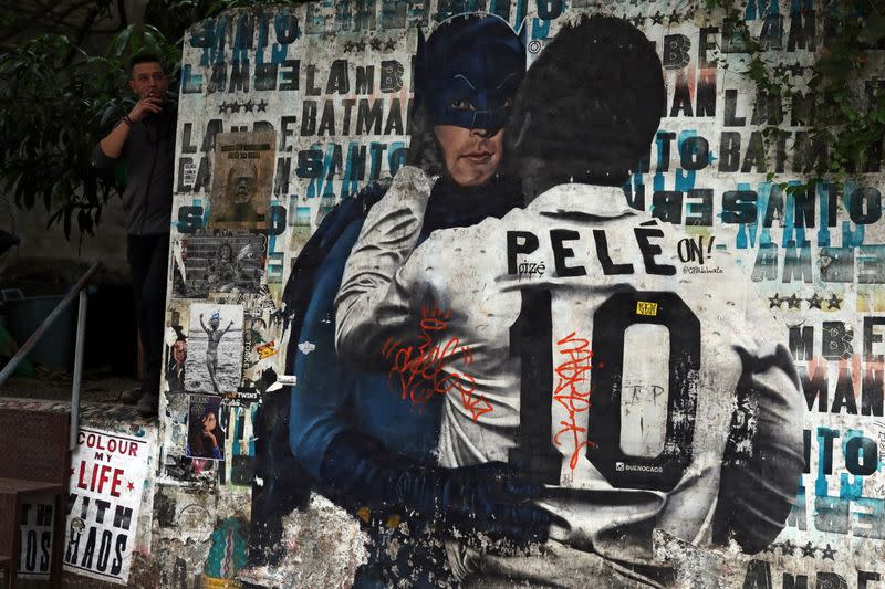 A man smokes near a mural depicting Brazilian soccer legend Pele kissing the face of comic superhero Batman in Sao Paulo