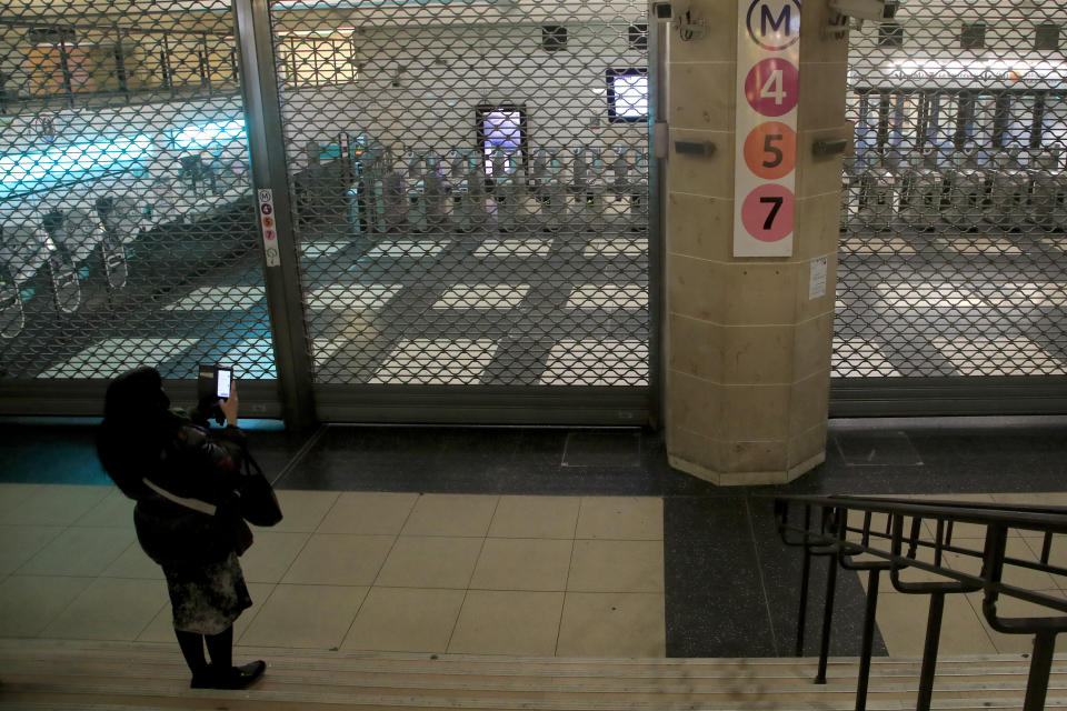 Una mujer toma fotos del acceso cerrado al Metro de París, viernes 13 de diciembre de 2019. El presidente Emmanuel Macron dijo el viernes 13 de diciembre de 2019 que quiere seguir adelante con la reforma del sistema jubilatorio a pesar de las huelgas que se prolongan desde hace más de una semana. (AP Foto/Michel Euler)