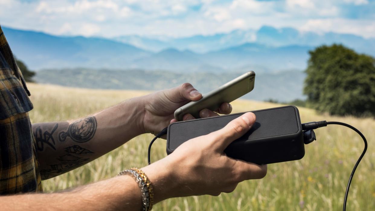  Man Using Portable Speaker Connected to Mobile Phone in Nature . 