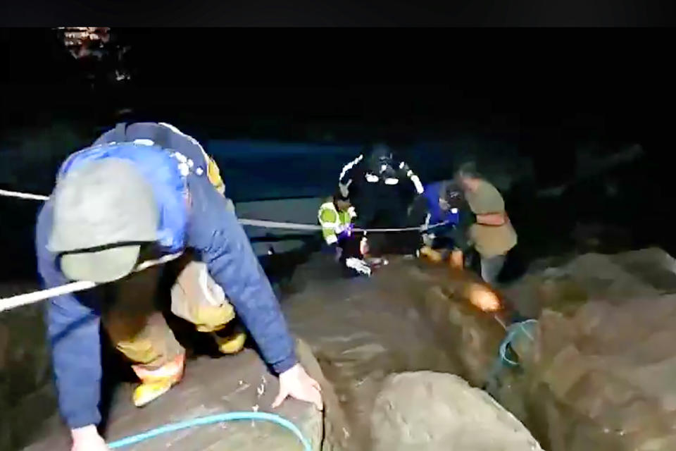 This photo from video provided by Rob Gensorek of Basin Tackle Charleston shows firefighters rescuing the crew from a capsized crab boat in the harbor at Coos Bay, Ore., late Tuesday evening, Jan. 14, 2020. Three men were in good condition early Wednesday after being cut from inside the hull of the capsized boat. The 38-foot (11-meter) Pacific Miner was flipped upside-down by large waves late Tuesday and then got caught on rocks in a jetty in Coos Bay as the tide went out. A U.S. Coast Guard helicopter on a routine training mission spotted the vessel and launched a rescue, the agency said in a news release. (Rob Gensorek of Basin Tackle Charleston via AP)