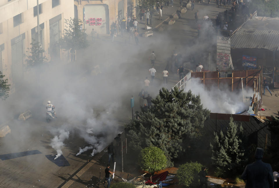 Hezbollah supporters run after tear gas is fired by riot policemen, near the government palace, in Beirut, Lebanon, Tuesday, Oct. 29, 2019. Lebanon's prime minister resigned, bowing to one of the central demands of the protesters. The news came shortly after baton-wielding Hezbollah supporters rampaged through the main protest camp in Beirut, torching tents and chasing away demonstrators. (AP Photo/Hussein Malla)