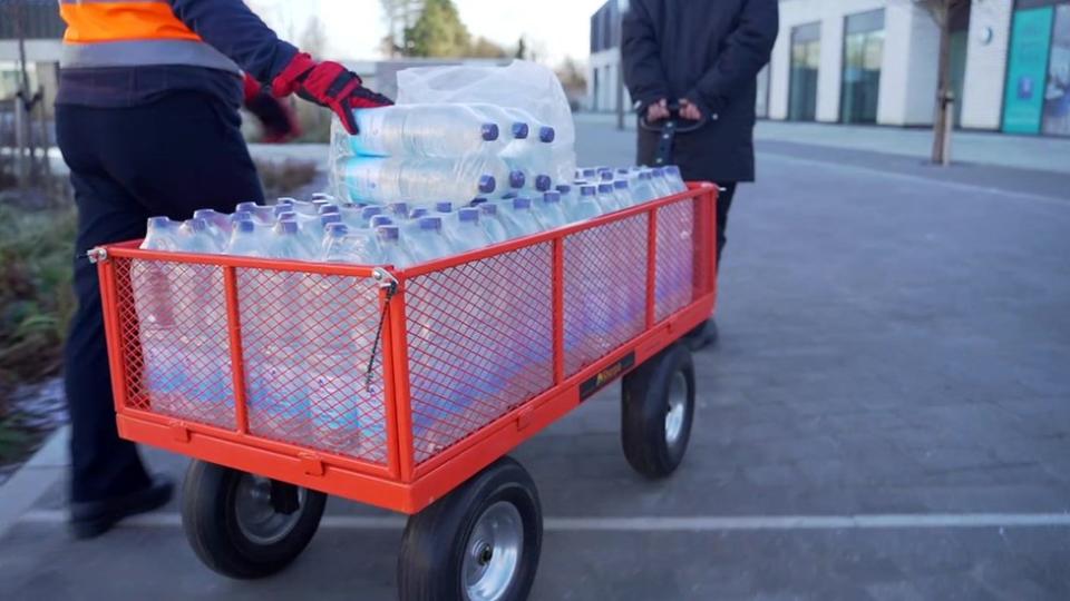 Two men are pulling a cart loaded with water bottles