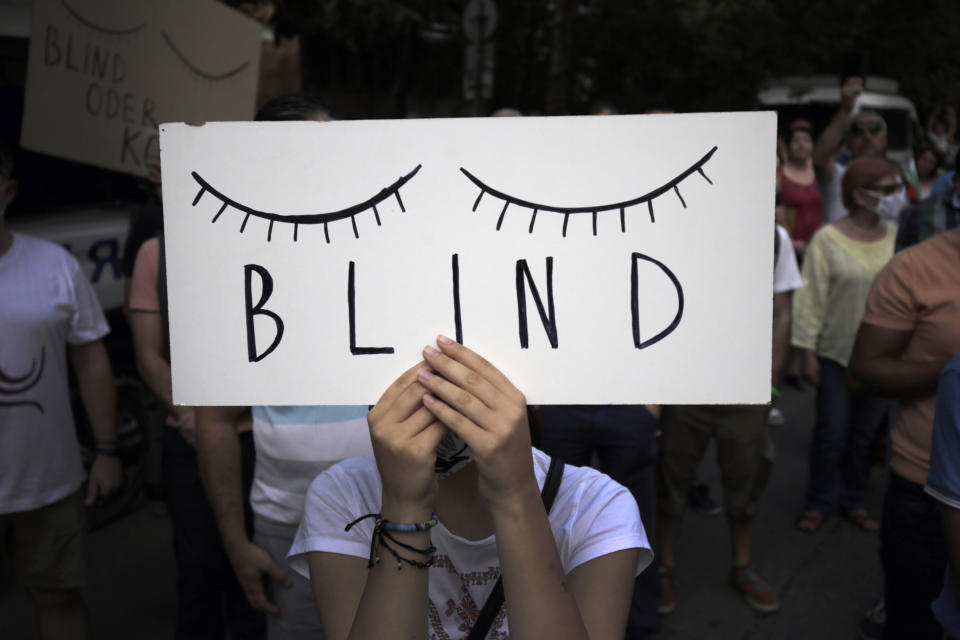 A protester holds a poster in front of the German Embassy in Sofia, Bulgaria, Wednesday, Aug. 12, 2020. Several hundred anti-government protesters gathered in front of Germany’s embassy in Sofia, calling on Berlin and Brussels to “open their eyes” to widespread corruption in Bulgaria. During the peaceful protest, dubbed “Eyes Wide Shut,” organizers complained that the European Union has willfully ignored the state of affairs in its poorest member state. (AP Photo/Valentina Petrova)