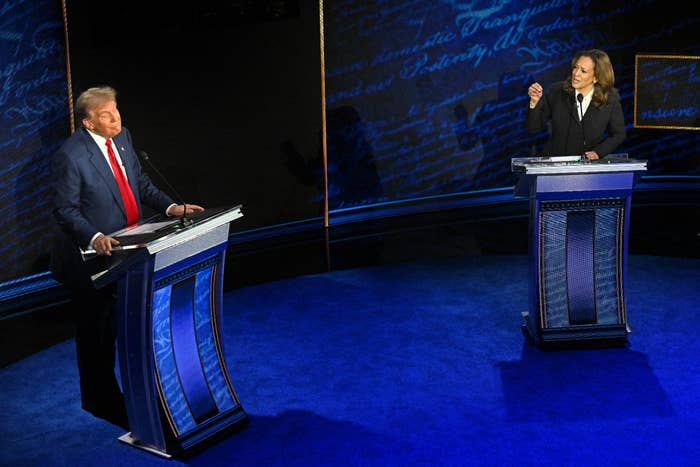 Mike Pence and Kamala Harris debate on stage, each standing at a podium. The background has text from historical U.S. documents