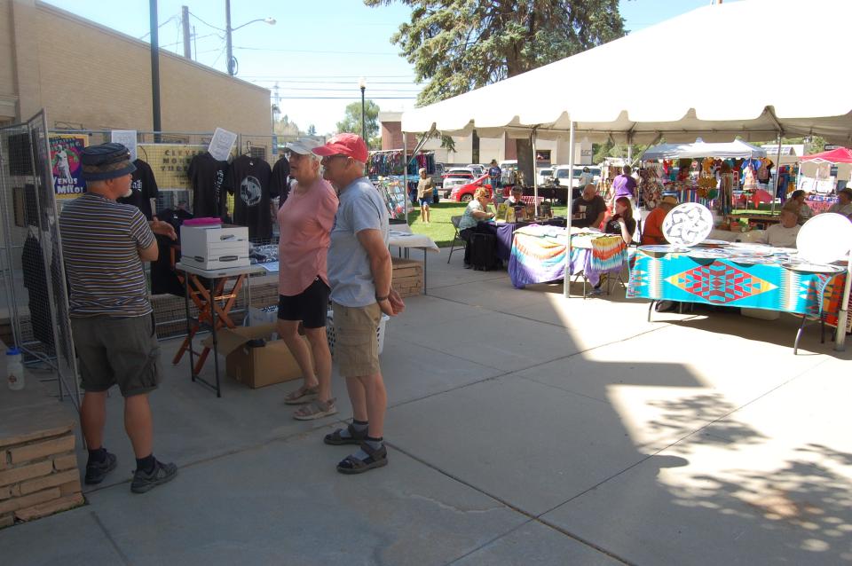 Artist Michael Darmody, left, visits with a couple of visitors to his space at the Makers Market in Orchard Plaza in downtown Farmington on June 2.