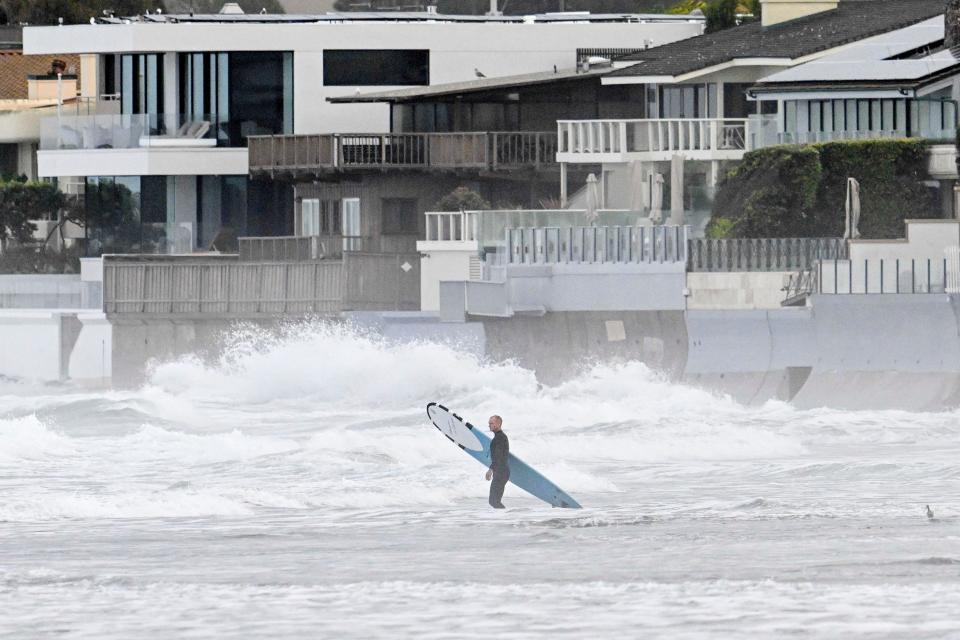 A surfer enters the water at La Jolla Shores Tuesday, Jan. 23, 2024, in La Jolla, Calif. California Gov. Gavin Newsom declared a state of emergency for San Diego County and Ventura County, which was also hit by heavy rains that caused flooding there in late December, stating that “I find that local authority is inadequate to cope with the magnitude of the damage caused by these winter storms.”