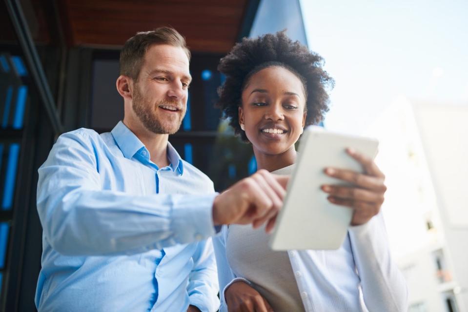 Two investors smile while looking at something on a tablet outdoors.