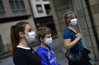 A family wearing face mask to protect of the coronavirus go for a walk, in Pamplona, northern Spain, Sunday, April 27, 2020. On Sunday, children under 14 years old will be allowed to take walks with a parent for up to one hour and within one kilometer from home, ending six weeks of compete seclusion. (AP Photo/Alvaro Barrientos)
