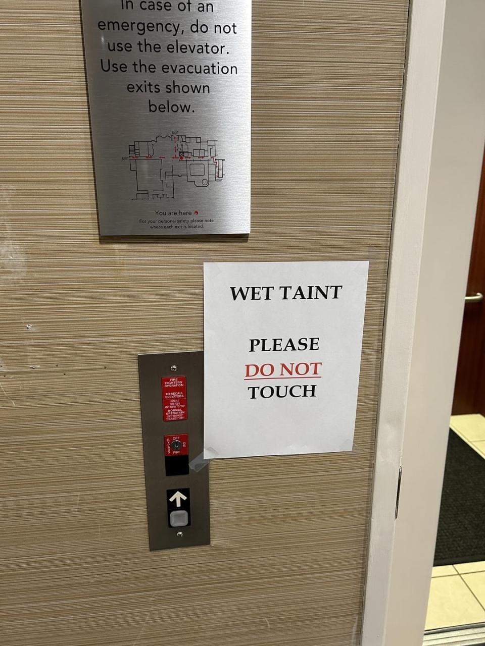 Sign next to an elevator reads "PLEASE T' AINT DO NOT TOUCH" with a diagram of evacuation routes above it