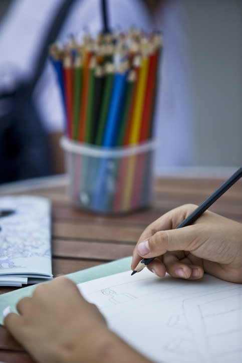 Person sketching on paper with pencils in background, depicting a creative work environment