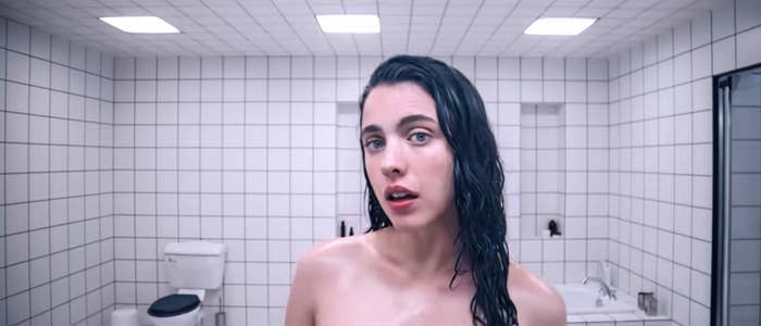 A person with wet hair stands in a tiled bathroom with a neutral expression