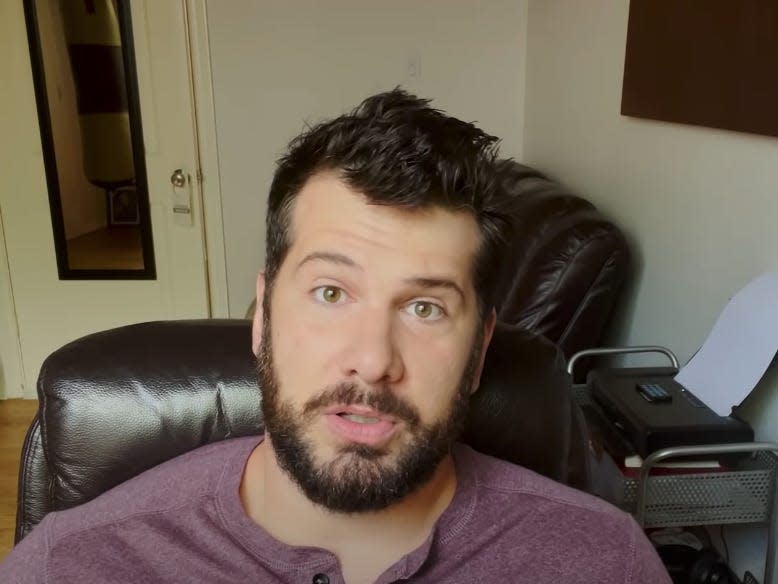 Steven Crowder sitting in a desk chair, looking at the camera with a couch behind him